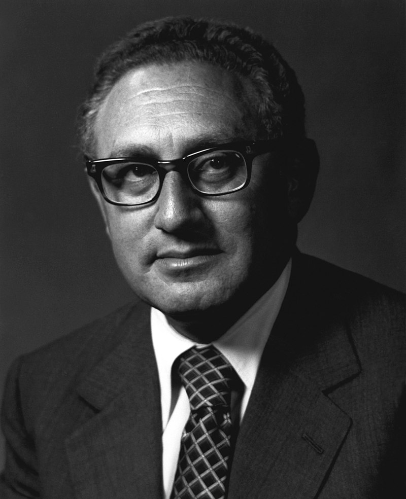 This is a picture of Henry Kissinger as a young man, in black and white. He is staring straight ahead at the photographer, possibly past the photographer. He has a neutral expression.